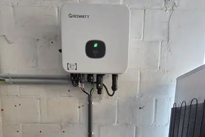 Thuisbatterij tegen een binnenmuur, met omvormer en bekabeling erboven.