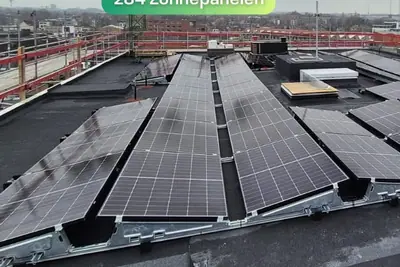 Rijen zonnepanelen op het platte dak van een nieuwbouwproject, met bouwkraan op de achtergrond.