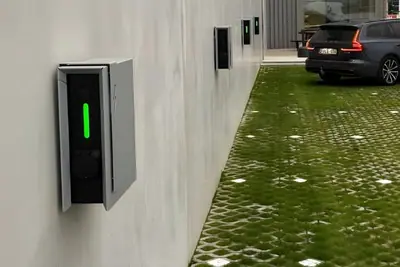 Wandlaadpunt op een bedrijfsgevel, met geparkeerde wagen op de parking ernaast.